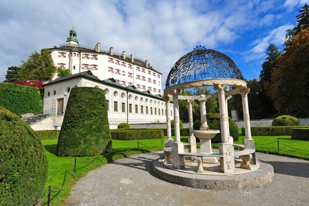 White Renaissance facade of Ambras Castle surrounded by manicured green lawns in Innsbruck, Austria