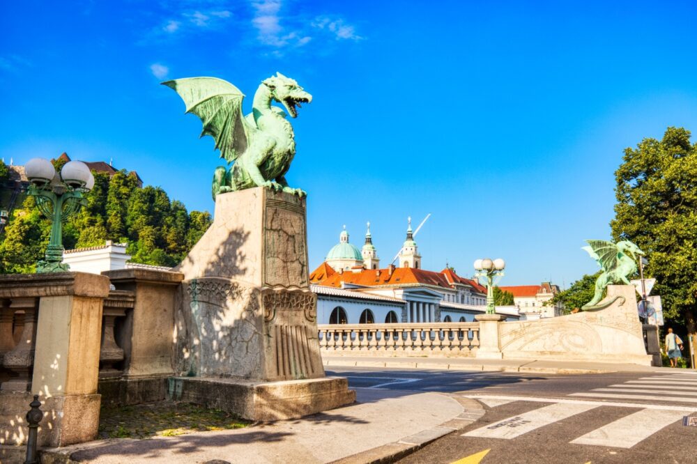 Green bronze dragon statue perched on the stone balustrade of the Dragon Bridge in Ljubljana, Slovenia