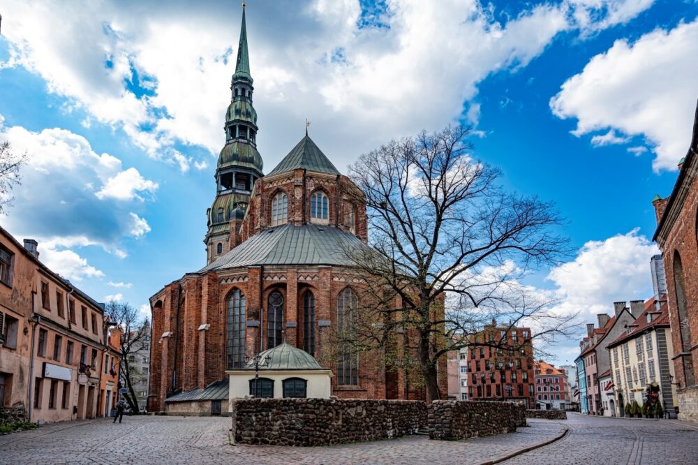 Brick Gothic facade and tall green spire of St Peter's Church on a cobblestone plaza in Riga, Latvia
