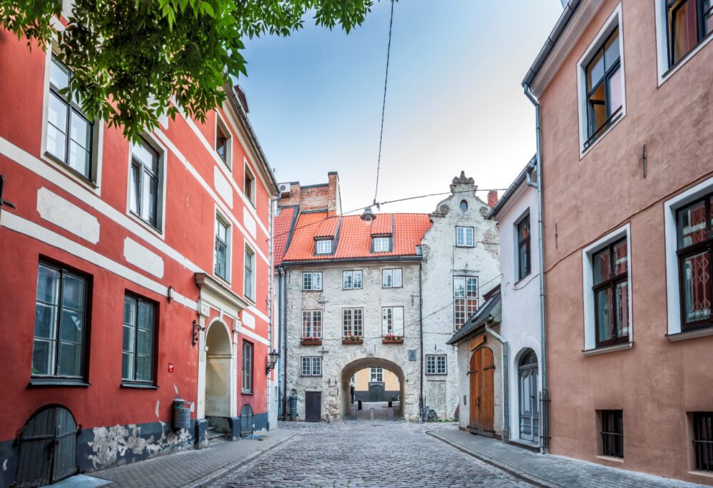 Cobblestone lane and red historic building leading through the medieval archway of the Swedish Gate in Riga, Latvia