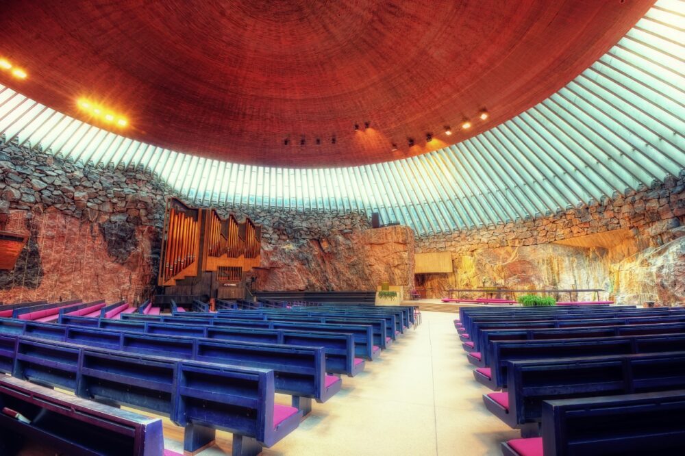Rough granite rock walls and circular copper-lined dome inside Temppeliaukio Rock Church in Helsinki, Finland