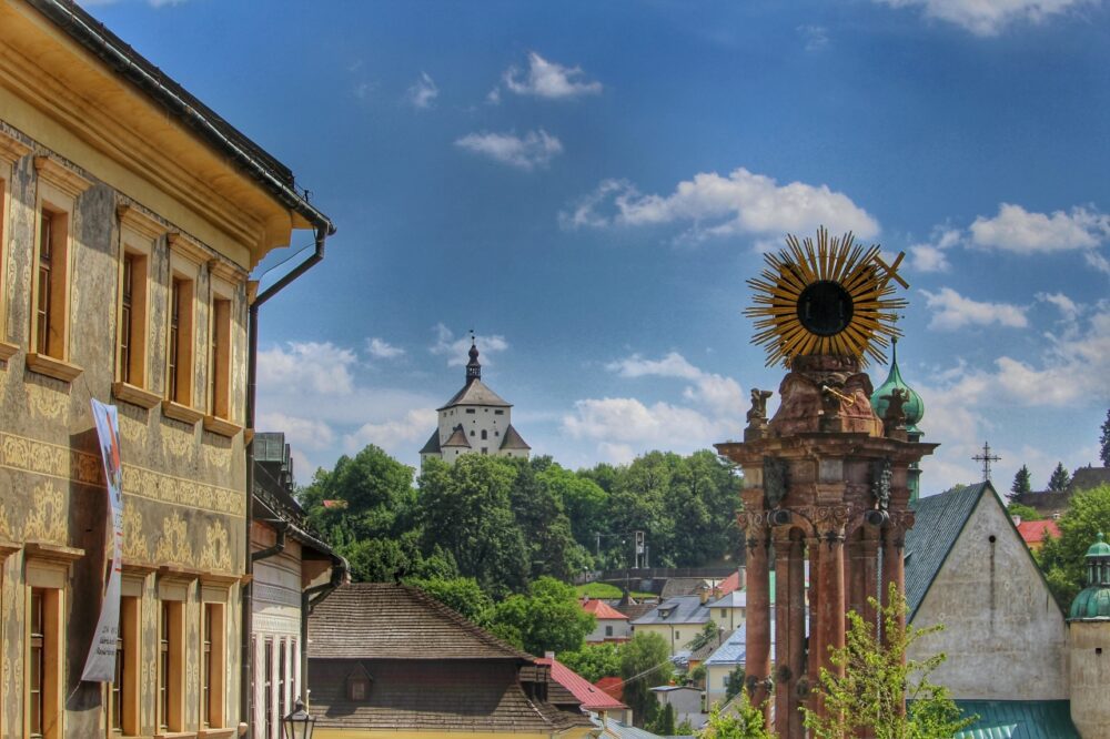 Ornate Baroque Holy Trinity Plague Column surrounded by pastel historic buildings in Banská Štiavnica, Slovakia