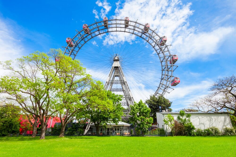 Red vintage cabins of the Wiener Riesenrad giant Ferris wheel rising above green trees in Prater Park, Vienna, Austria